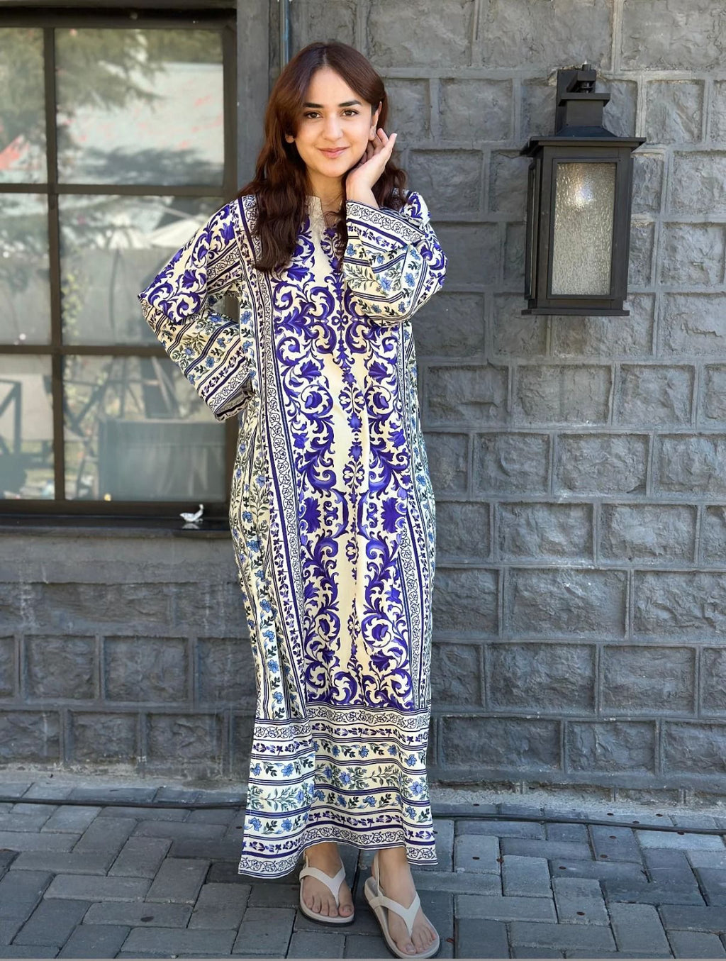 Woman wearing a patterned dress standing against a stone wall.