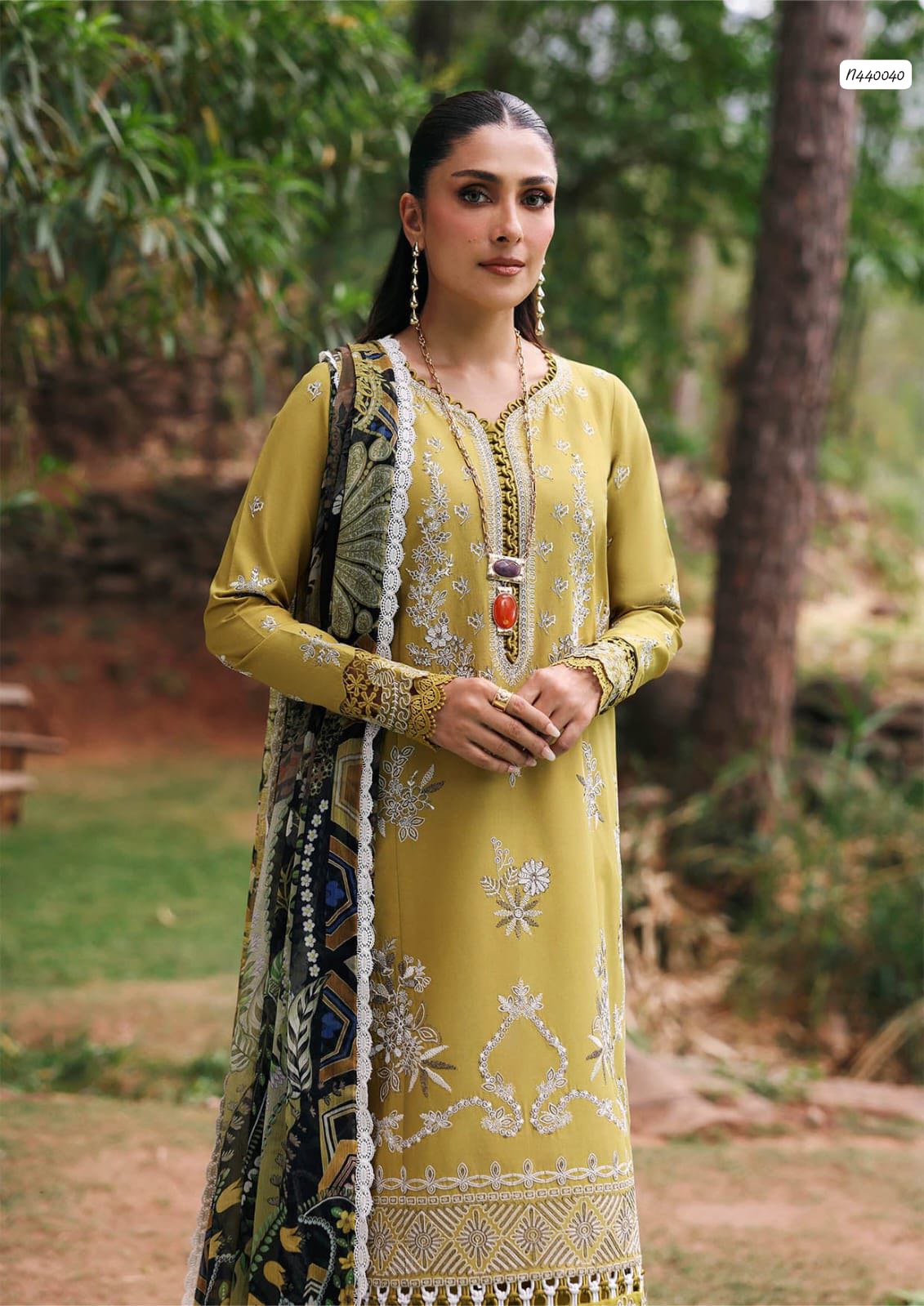 Woman in a yellow embroidered outfit standing outdoors with greenery in the background