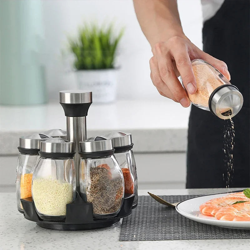 Person seasoning food with a spice rack containing various spices on a kitchen counter.
