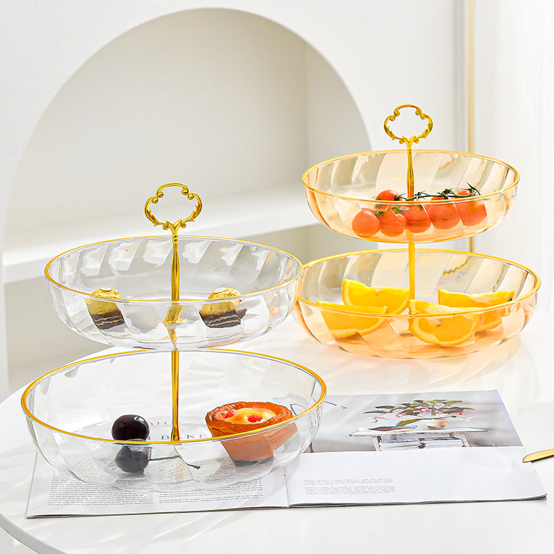 Three-tiered glass fruit basket with gold accents on a white surface.