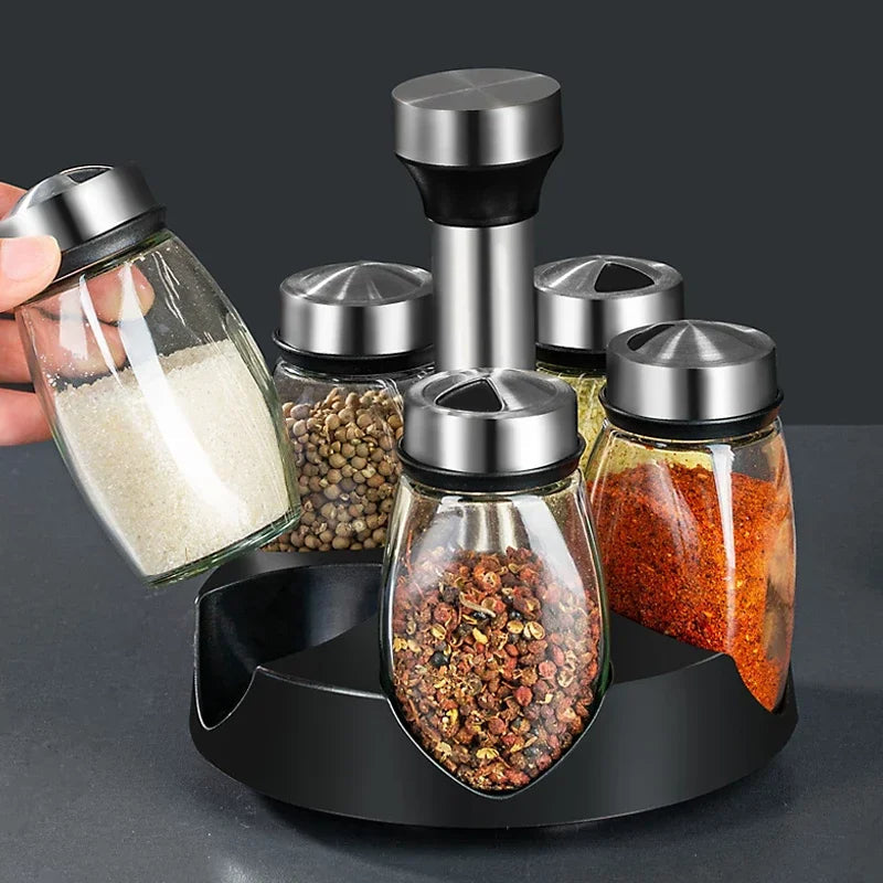Set of glass spice jars with metal lids on a black stand against a dark background