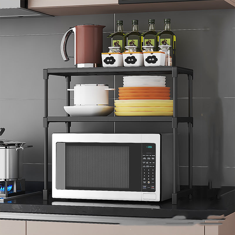 Kitchen shelf with microwave, cookware, and bottles against a gray tiled wall.