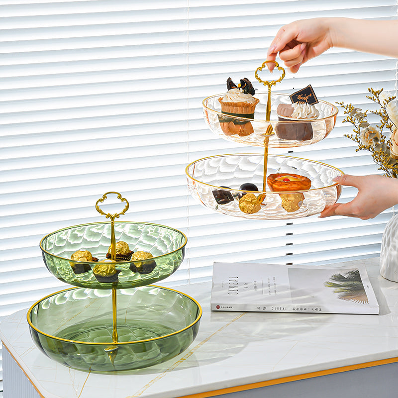 Three-tiered glass dessert stand with gold accents on a table, filled with small pastries.