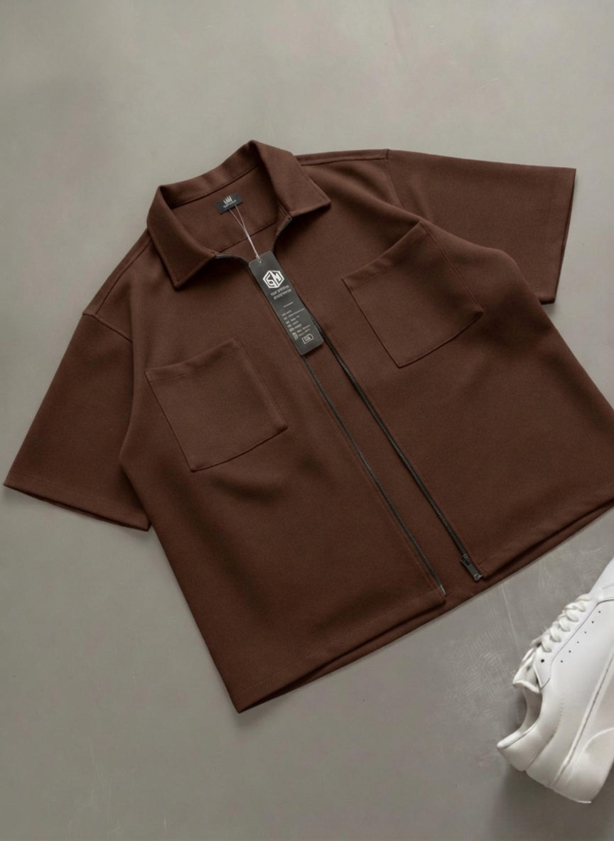Brown jacket with a tag on a gray surface, next to a white sneaker.