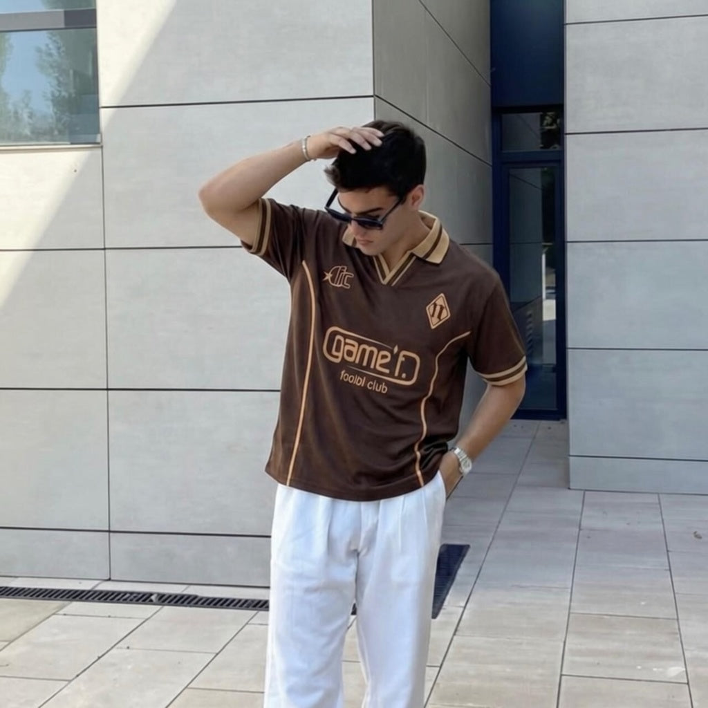 Person wearing a brown sports jersey with visible branding, standing against a modern building.
